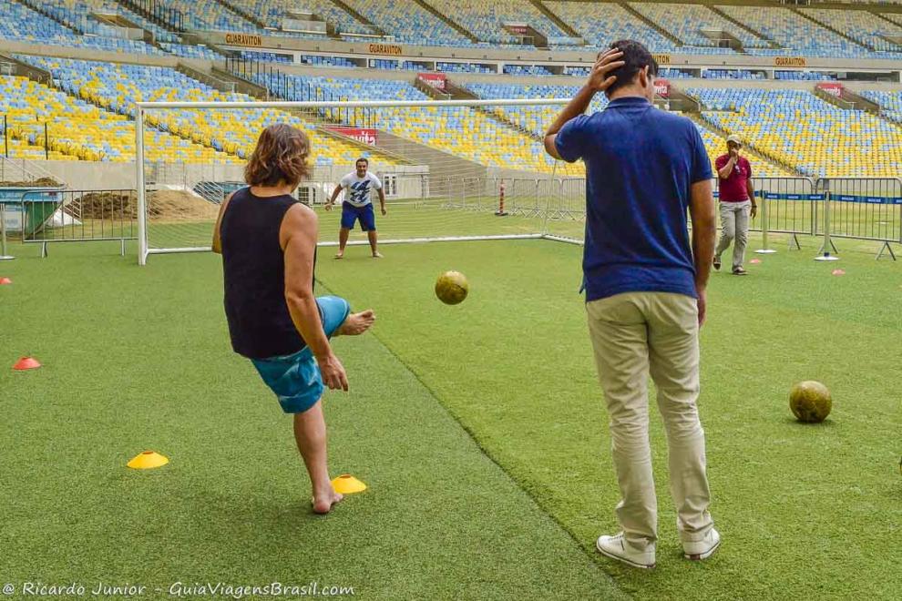 Imagem de pessoas no gramado do Maracanã chutando bola no gol.